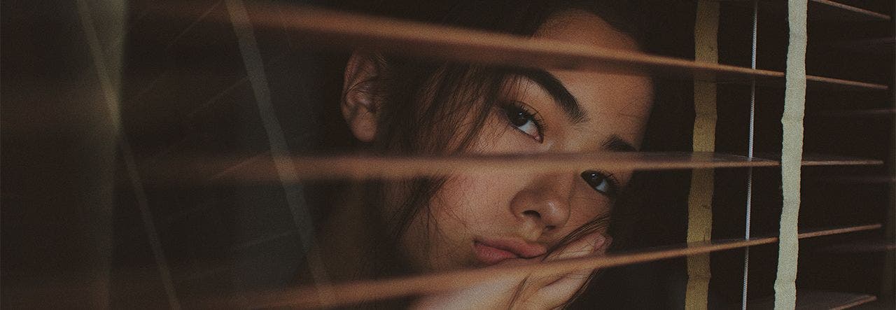Woman looking out of her window through the blinds