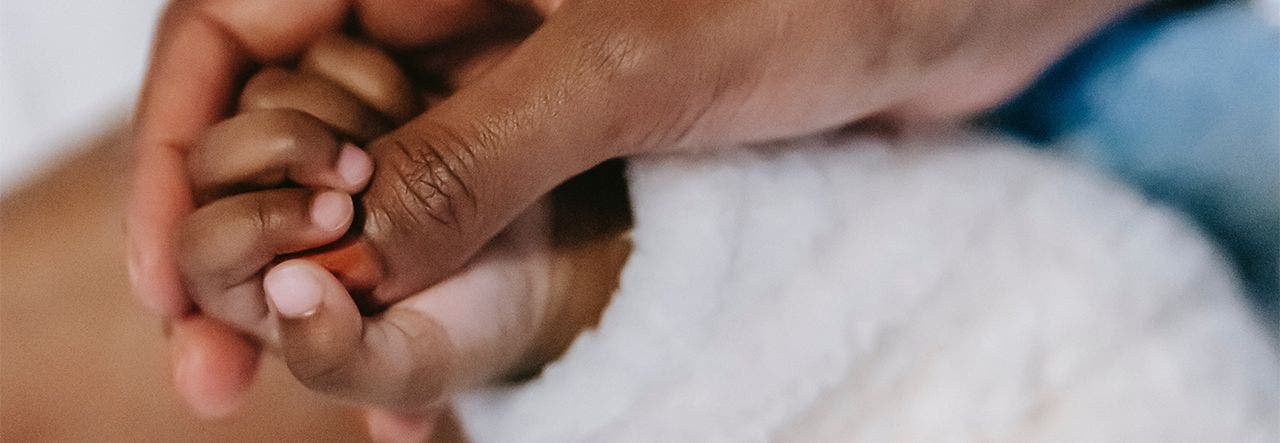 Baby's small hand holding onto their mother's thumb