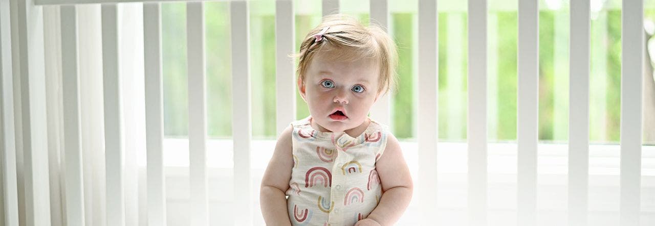 Toddler in a rainbow outfit sitting up on her mattress