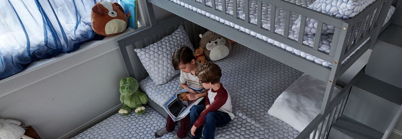 Two kids looking at a book together on a bottom bunk bed 