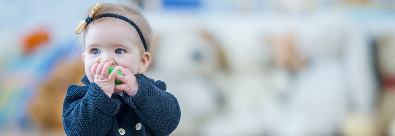 Toddler girl in a blue coat, using a non-toxic teething toy