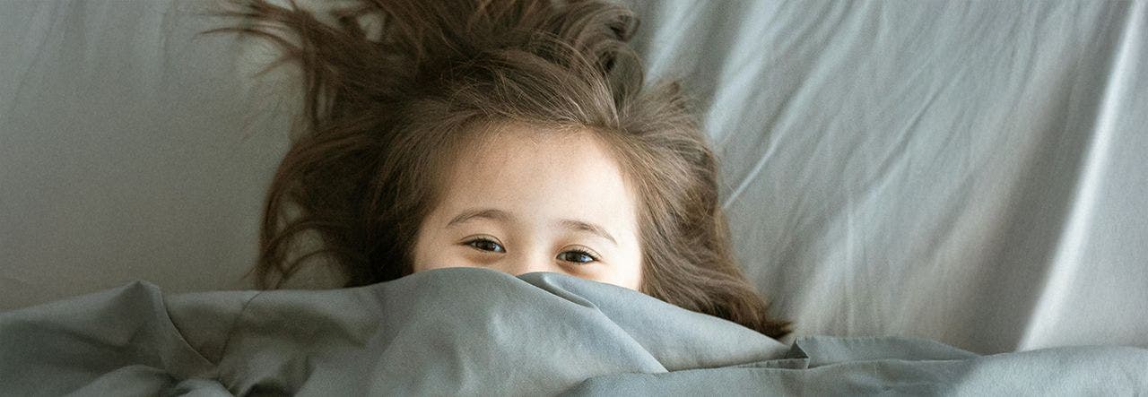 Child laying in bed under the covers