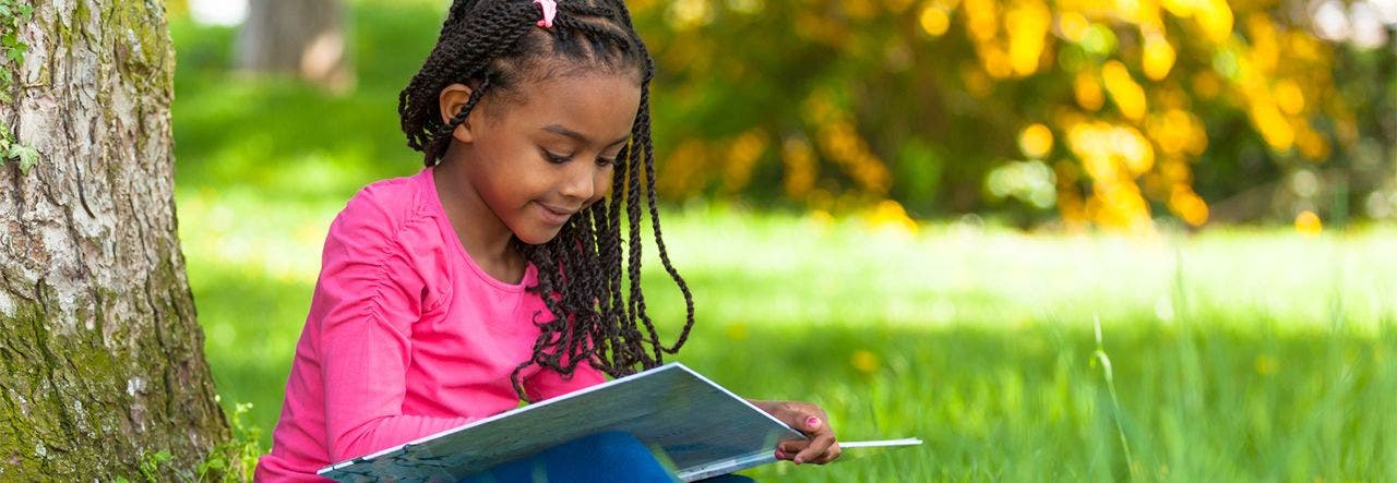 Little girl with braids reading a book outside