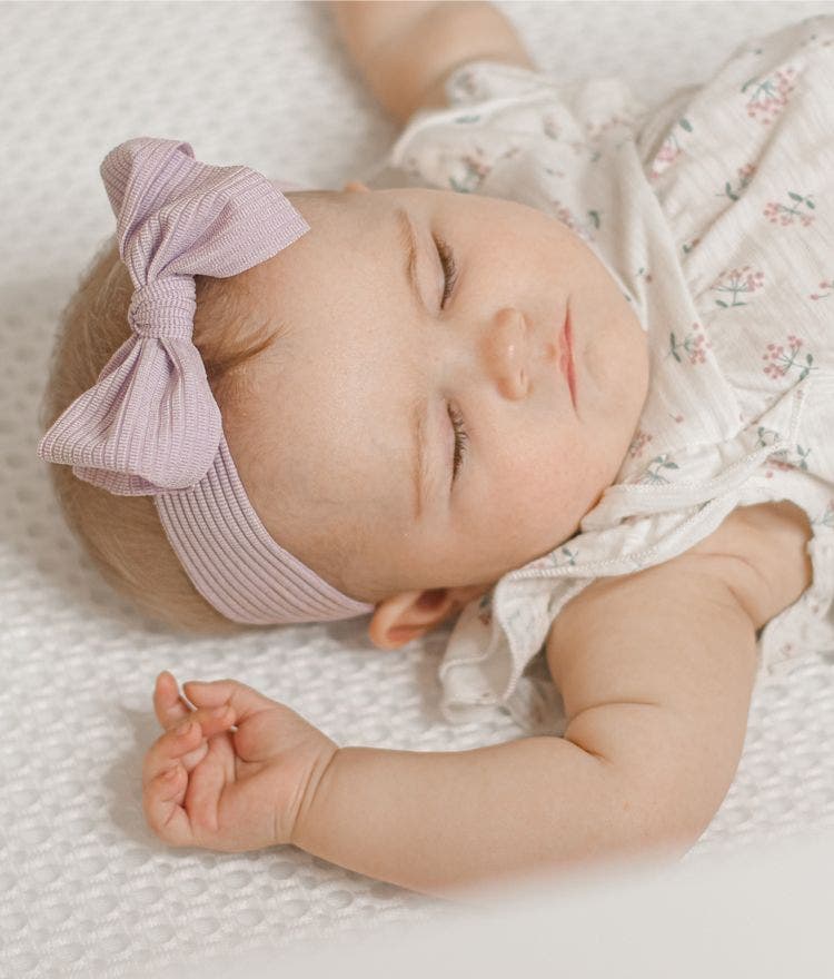 baby with bow sleeping on breathable crib mattress
