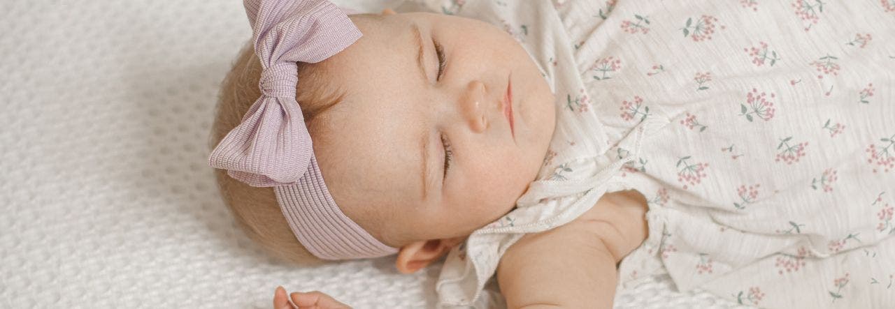 baby with bow sleeping on breathable crib mattress