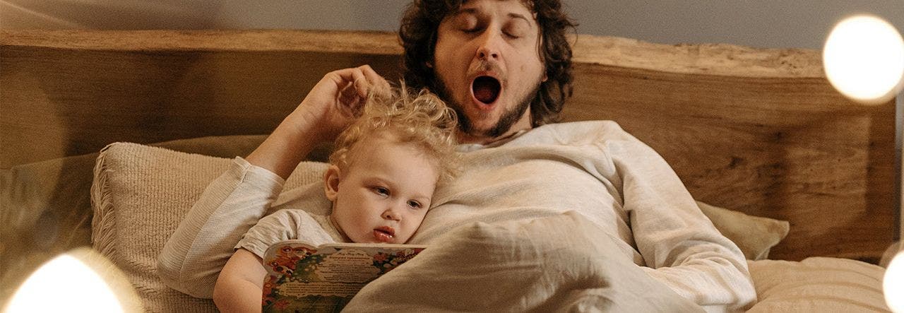 Father yawning while reading a bedtime story to his toddler