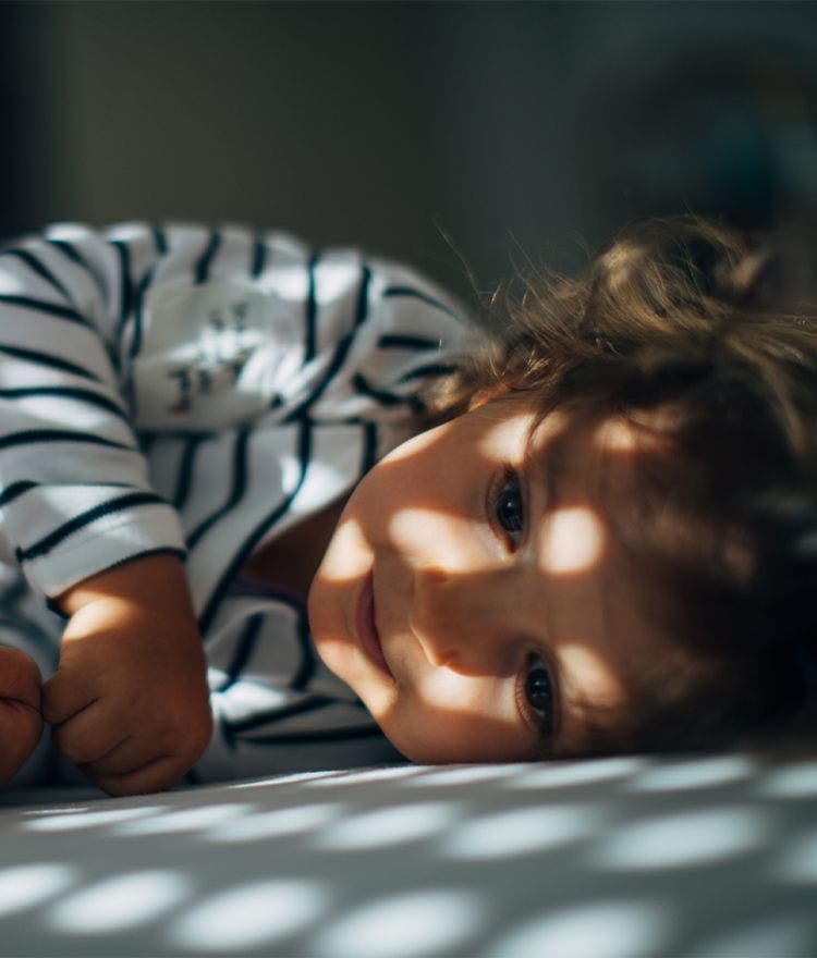 child sleeping in bed with light peeking through the blinds