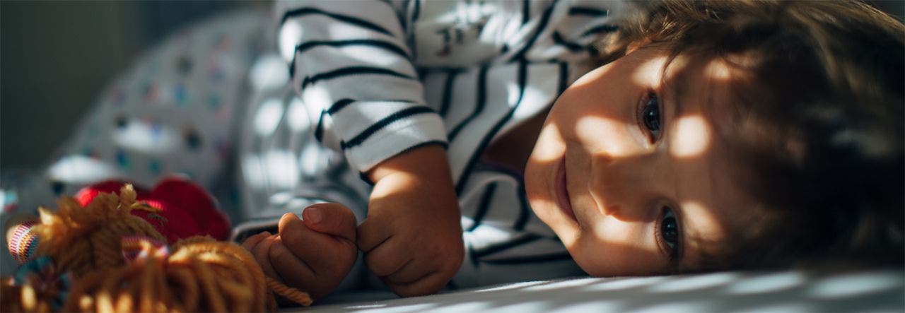 child sleeping in bed with light peeking through the blinds