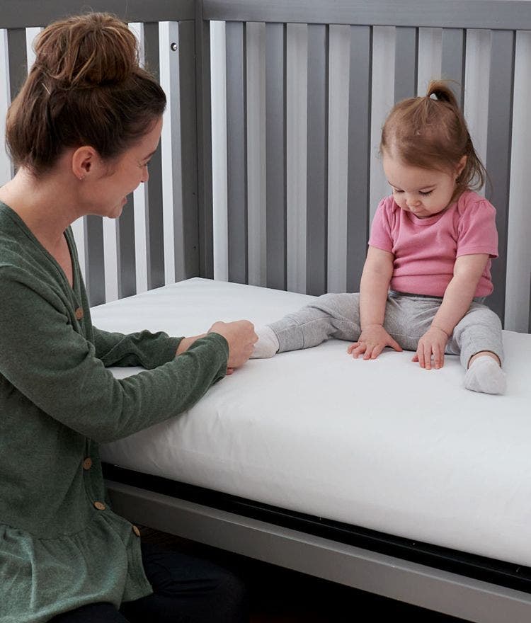 parent and toddler sitting on a lullaby earth crib mattress