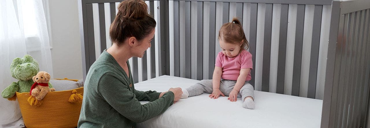 parent and toddler sitting on a lullaby earth crib mattress