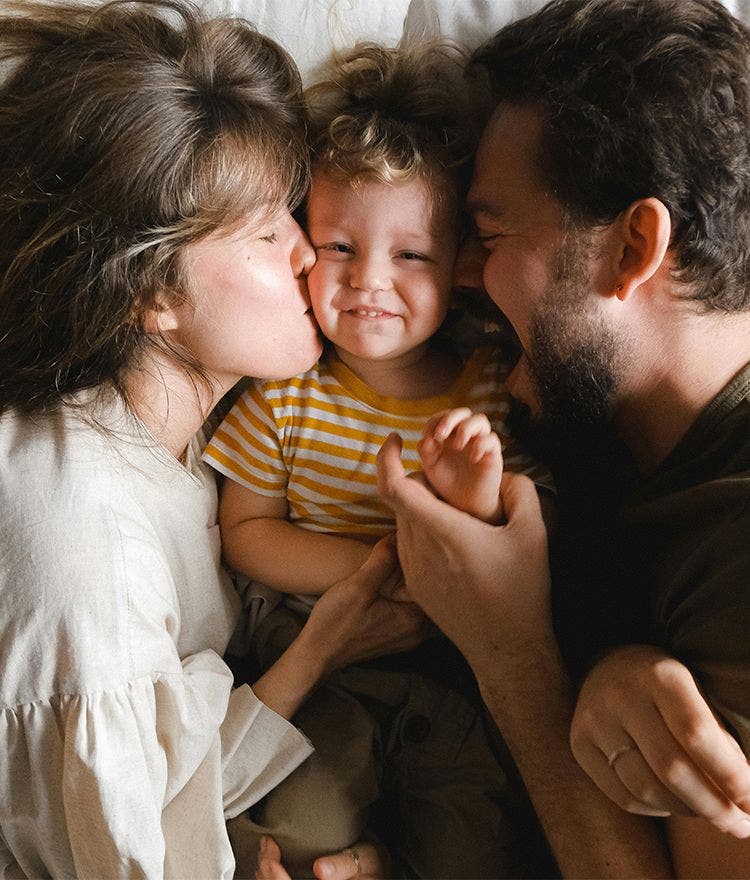 family of three laying in bed cuddling