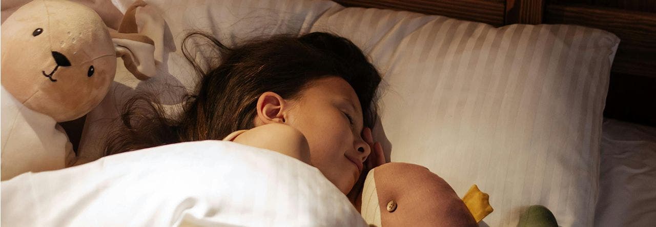 kid sleeping in bed with stuffed toys