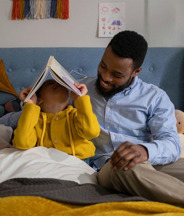 cild holding book over their face sitting with parent