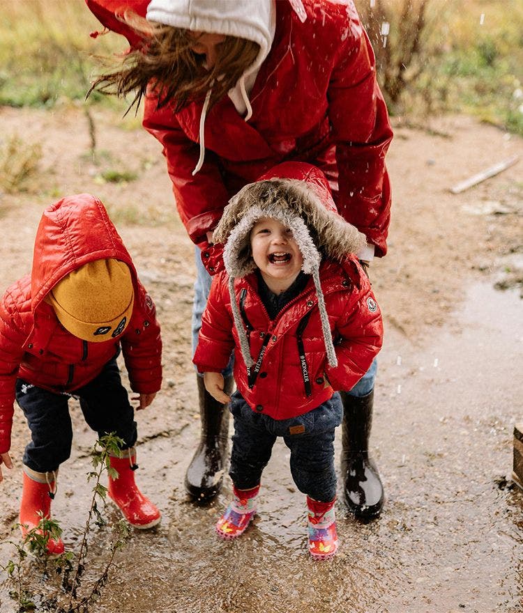children and parent in red raincoats jumping in puddles