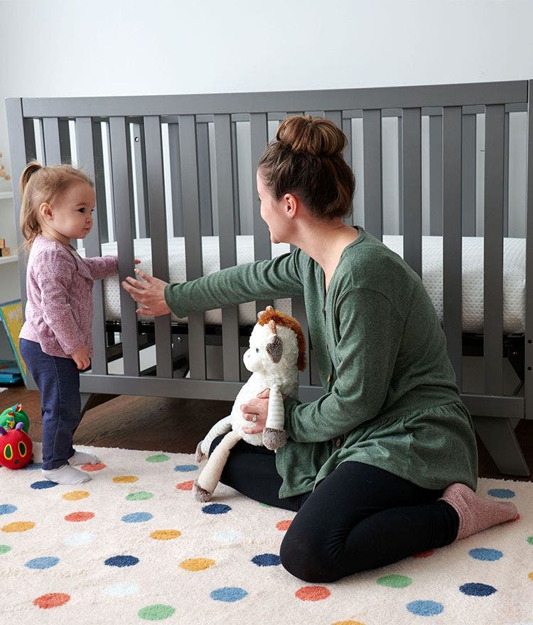 Woman and toddler sitting on ground in front of crib