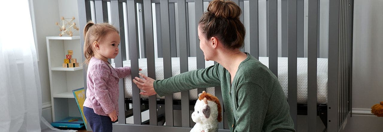 Woman and toddler sitting on ground in front of crib