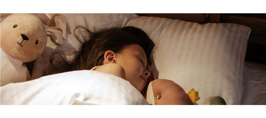 kid sleeping in bed with stuffed toys