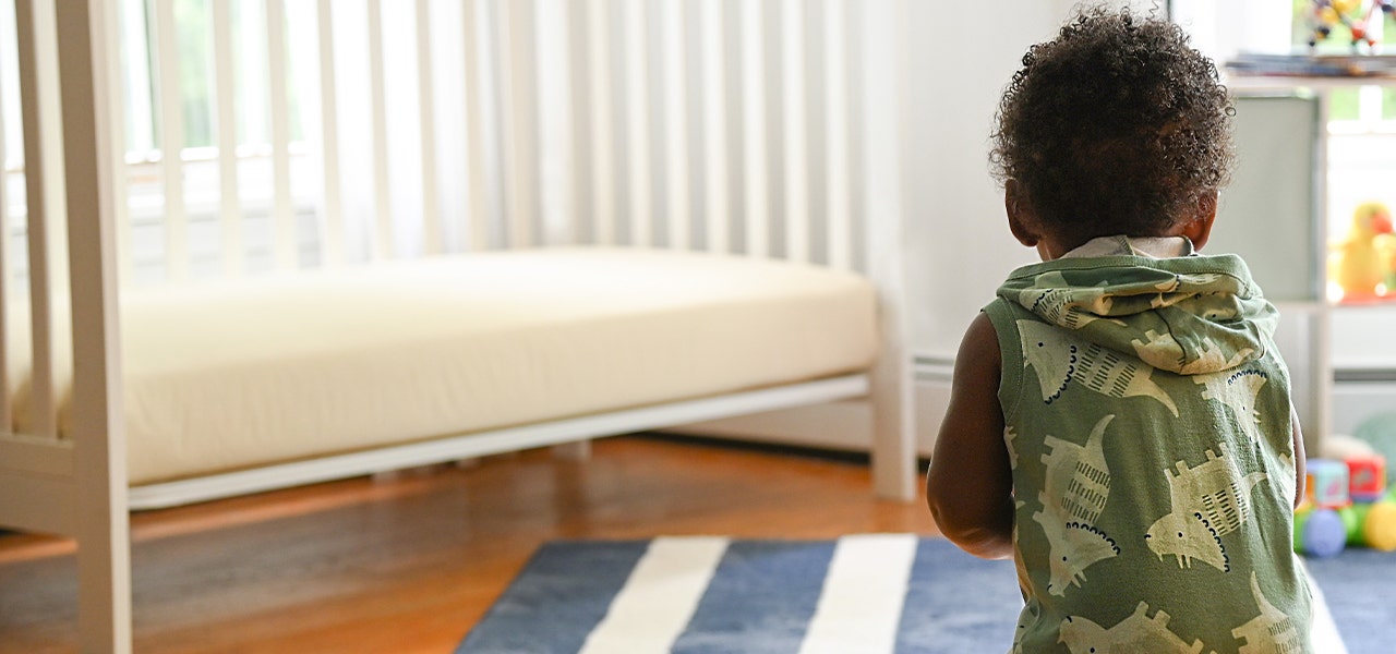 Toddler walking toward his crib with its Lullaby Earth non-toxic crib mattress