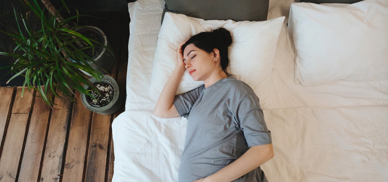 Pregnant woman sleeping on her side with her hand on her forehead