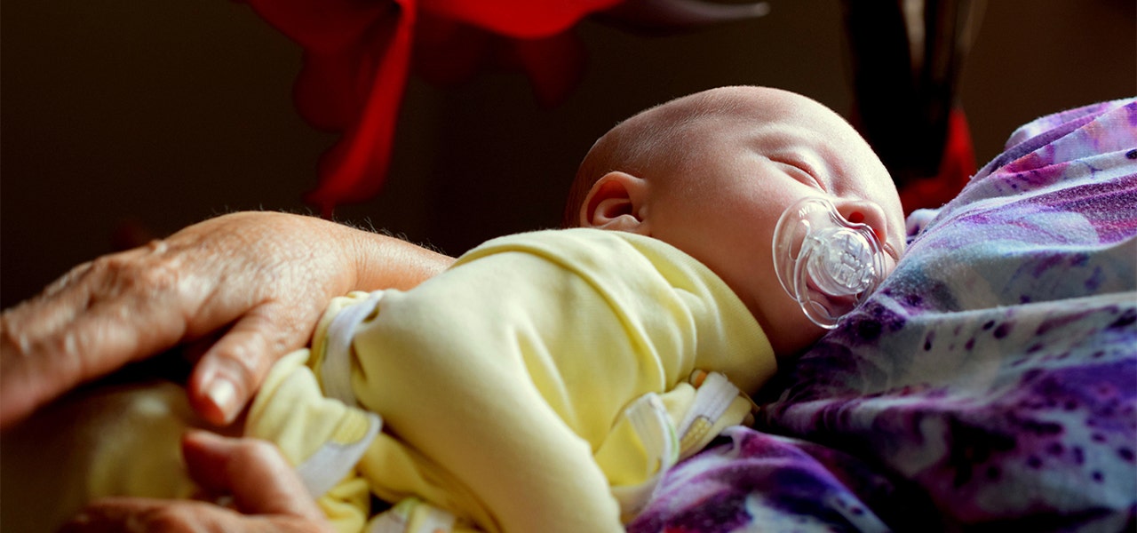 Sleeping baby wrapped in a swaddle and in their parent's arms