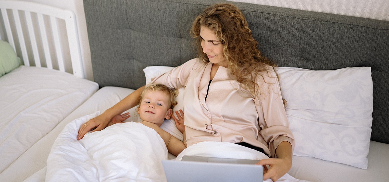 Mother and toddler awake in bed, mother with laptop in lap