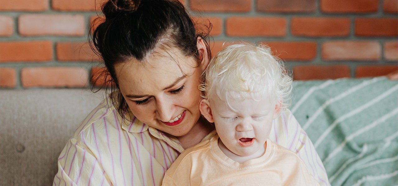 Teething toddler yawning in their mother's lap