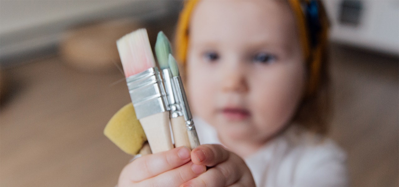 Toddler holding up several paint brushes
