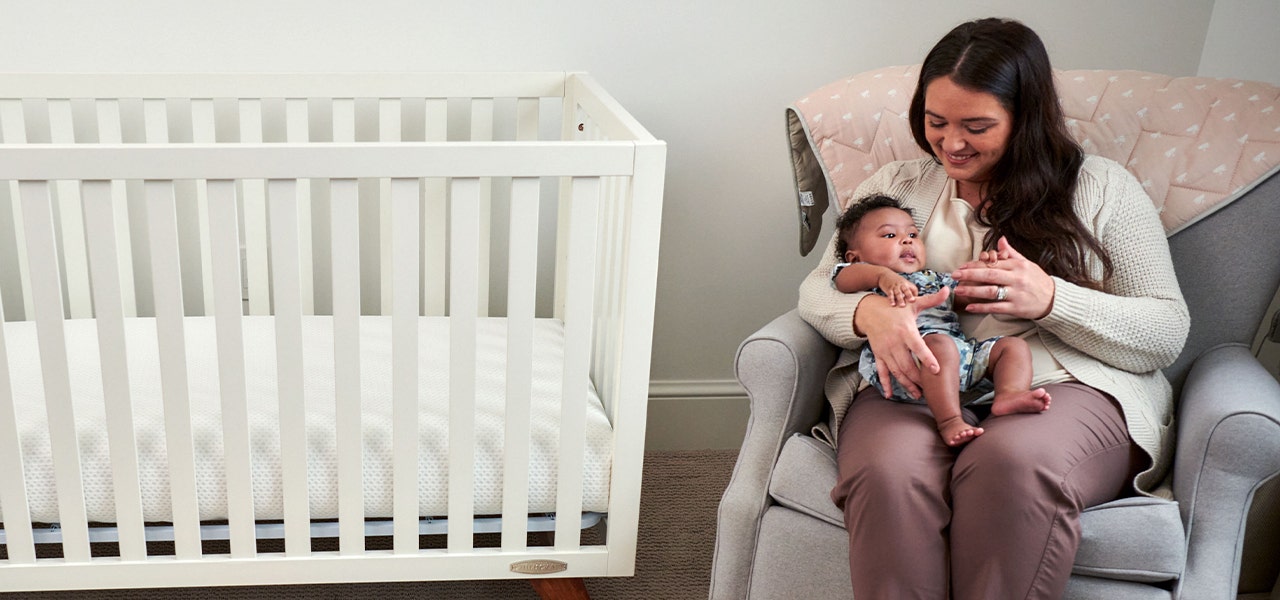 Mother cuddling her baby in a chair near the crib
