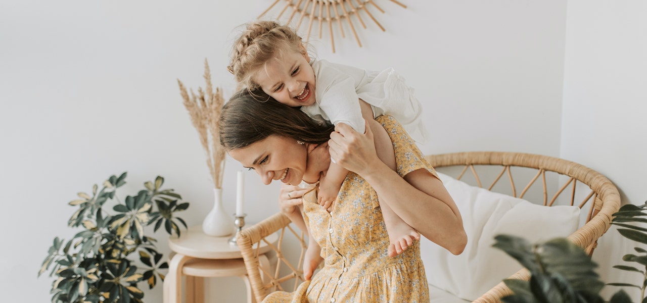 Toddler jumping on Mom's back and laughing in a fresh, clean home