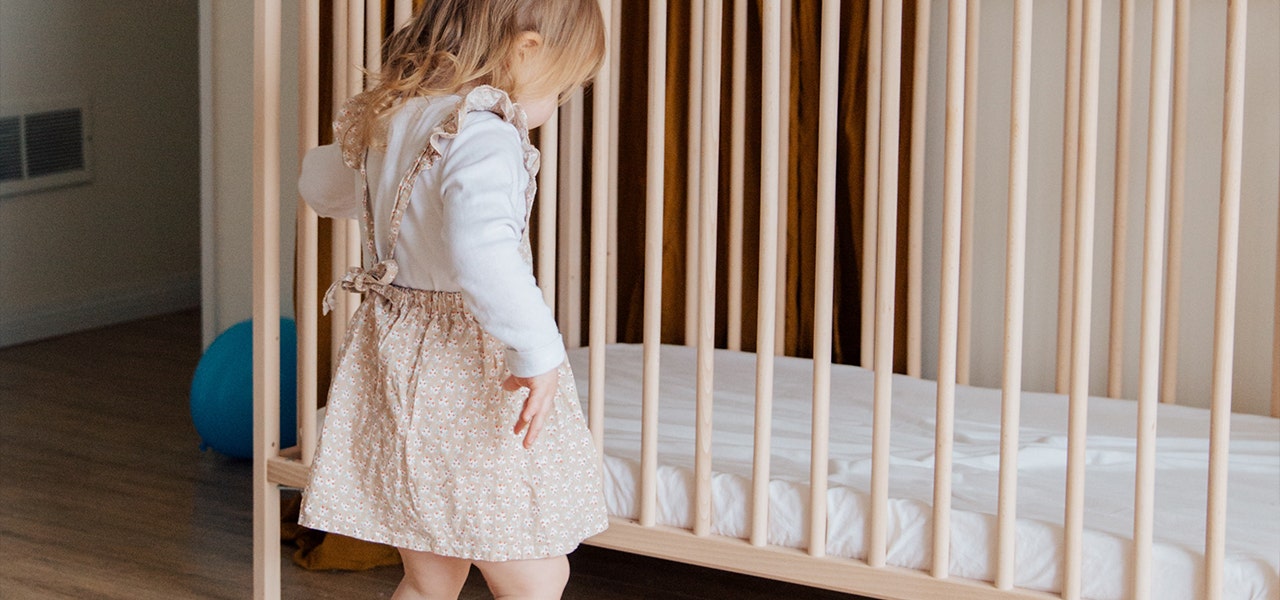 Toddler standing next to her crib, which is on the lowest setting