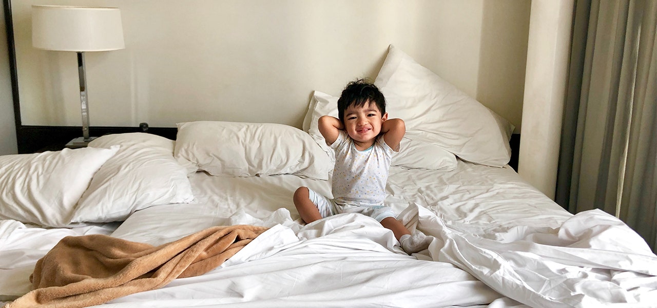 Toddler sitting up in a double bed and stretching