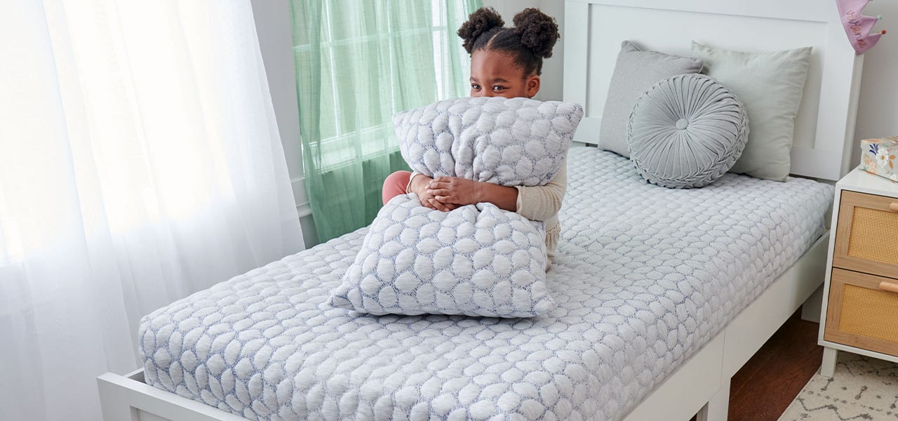 Young girl kneeling on her bed and hugging her pillow