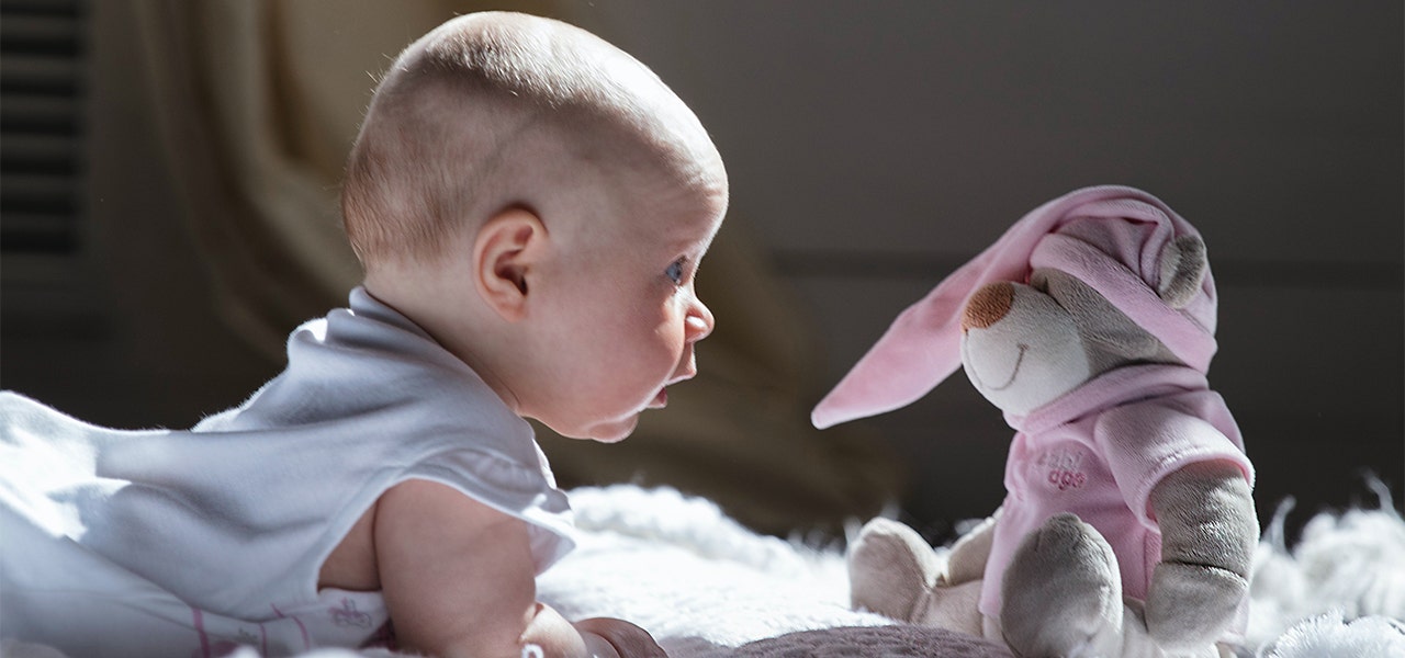 Wide awake baby enjoying tummy time with a stuffed bear