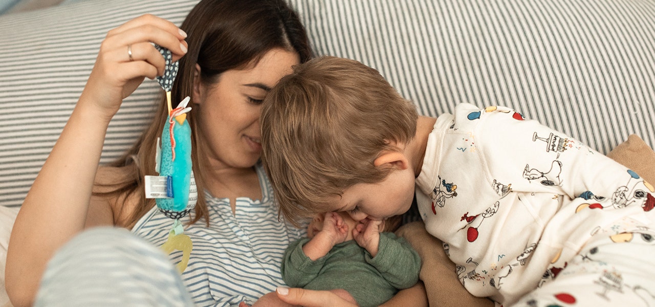 Mom holding a favorite toy while an older sibling snuggles Baby