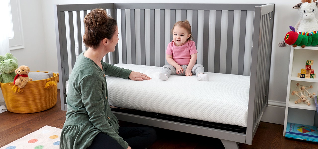 Toddler sitting up on a Lullaby Earth mattress, mother sitting nearby