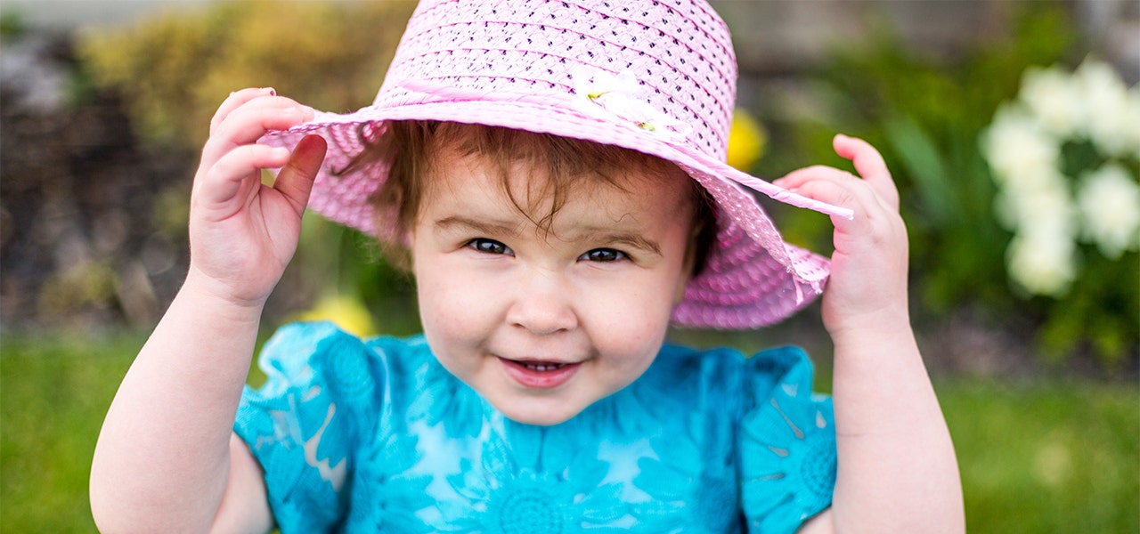 Toddler smiling outside and wearing a sunhat