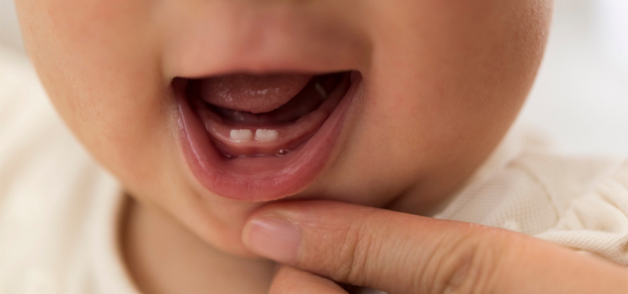 Parent pulling down Baby's lower lip to reveal new teeth