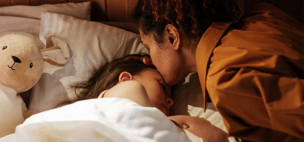 parent kissing child's forehead in bed