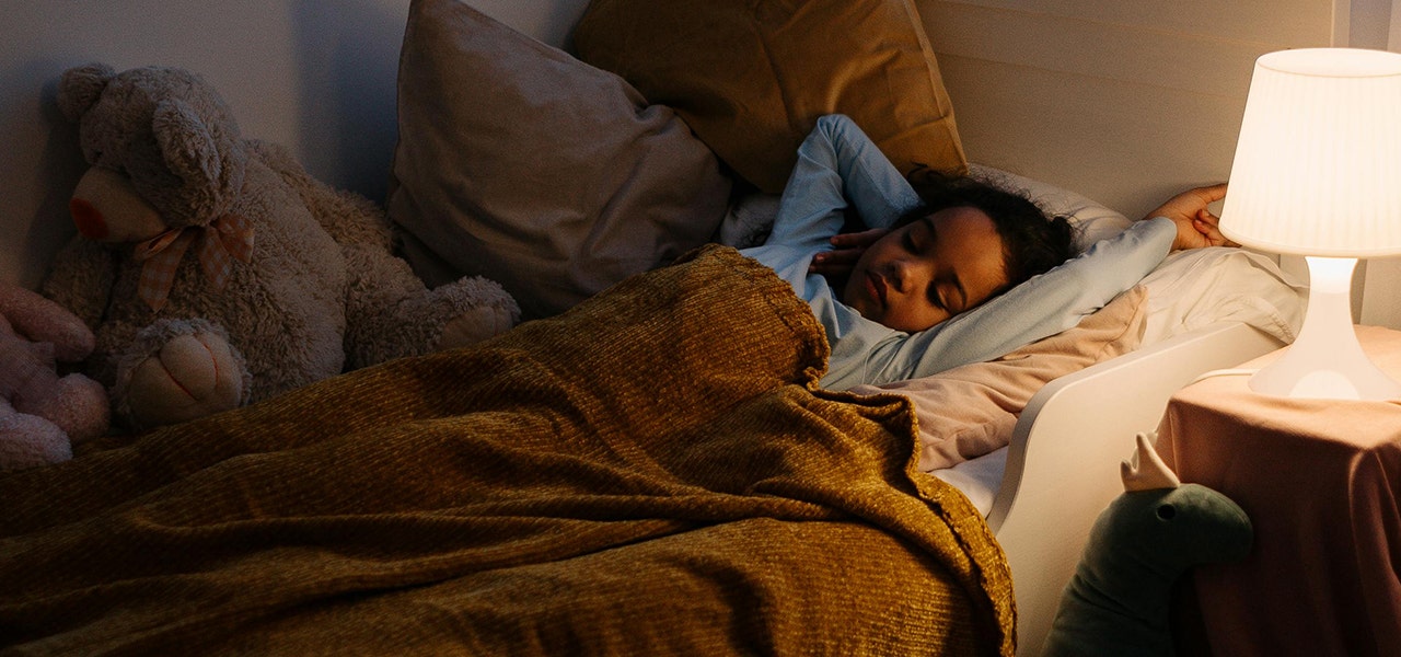 child sleeping in bed with bedside lamp