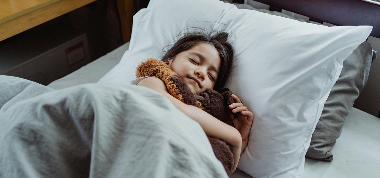child snuggling stuffed toy sleeping in bed