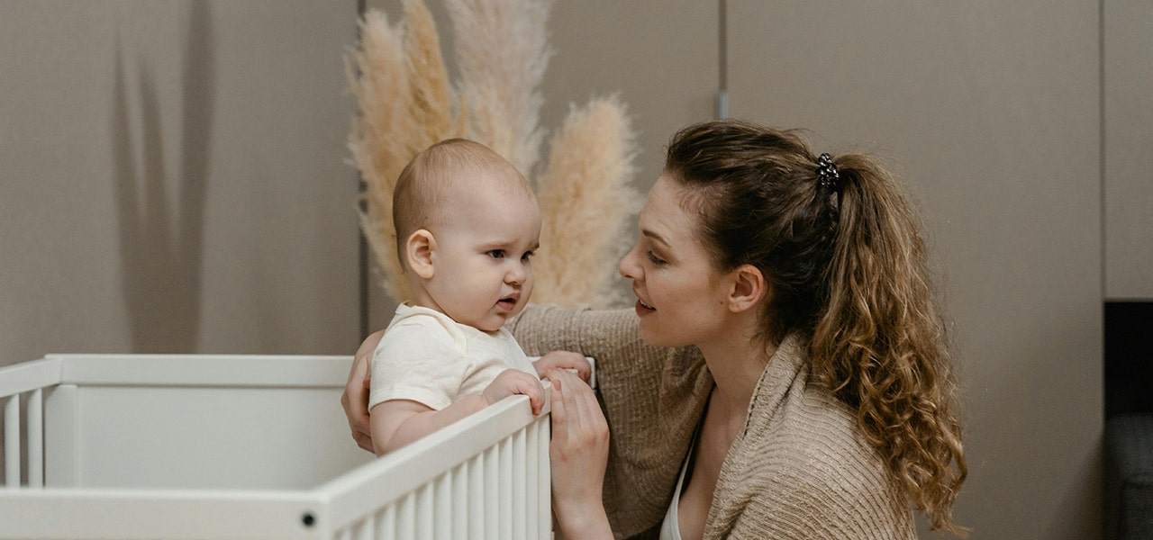 parent talking to toddler who is standing up in their crib