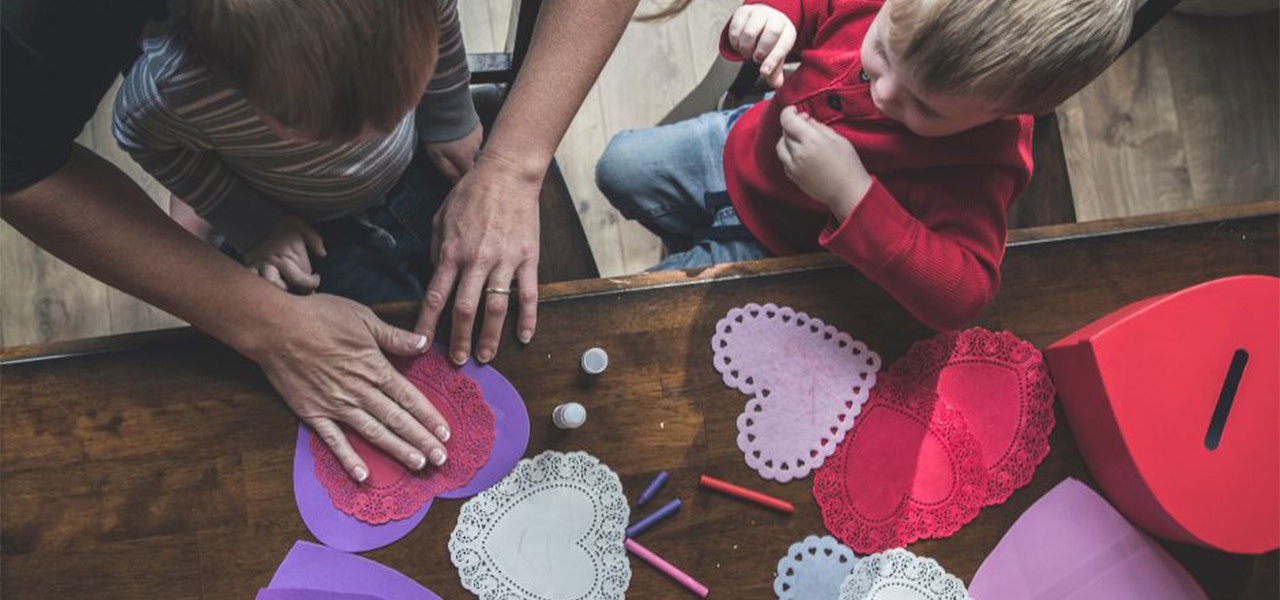 Parent helping two small children make heart-shaped Valentine's
