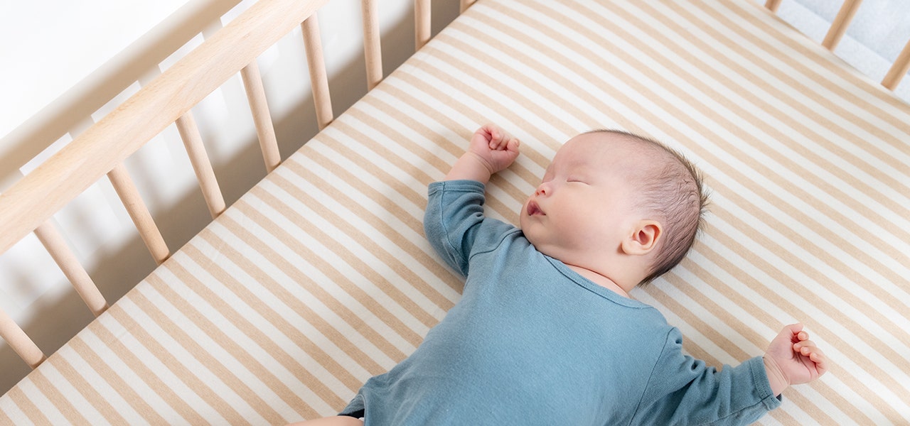 baby in blue onesie laying on crib mattress asleep