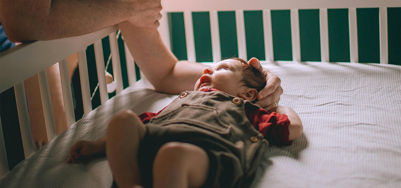parent embracing baby's head while they are laying in crib