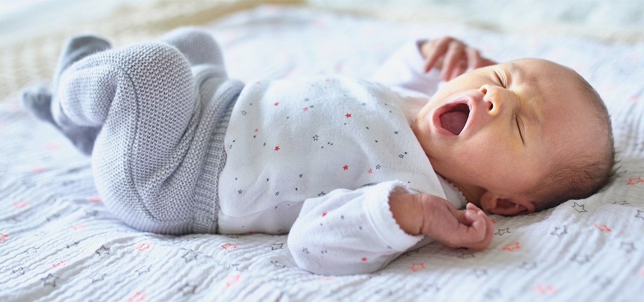baby yawning while laying on its back in its crib