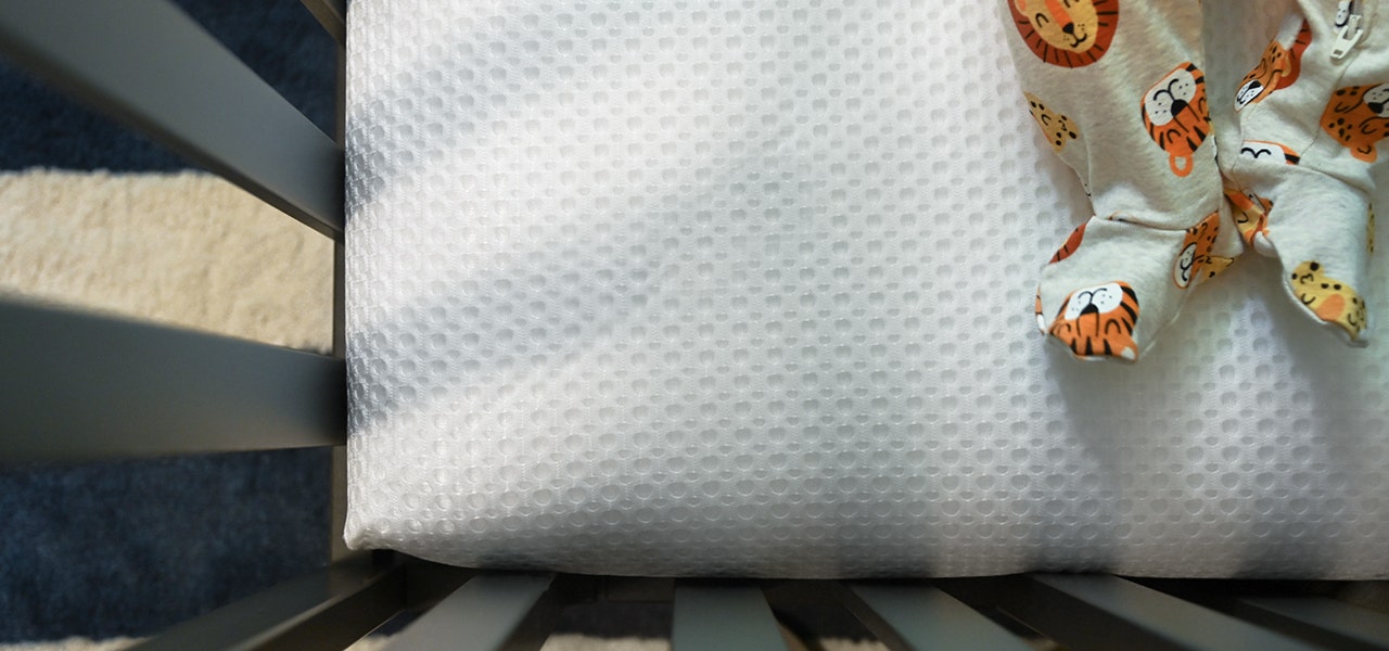 closeup image of lullaby earth crib mattress breathable cover with baby's feet in pajamas